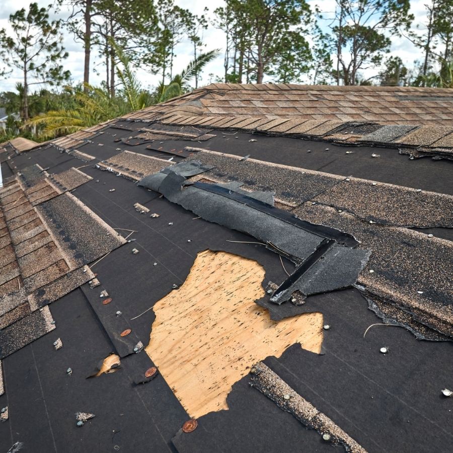 damaged house roof with missing asphalt shingles after storm